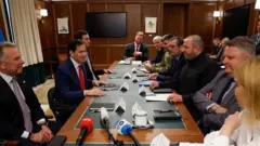 細長いテーブルで相対したアメリカとウクライナの代表団。ウクライナ外務次官は米特使の前に座り、腕を組んでいる