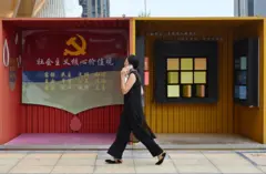 2024年9月20日，一名女子走過中國浙江省義烏市一家商業中心旁印有共產黨徽和口號的攤位。