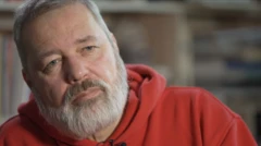 Gros plan Dmitry Muratov, rédacteur en ched de Novaya Gazeta. Un micro cravrate est accroché à son pull orange. 