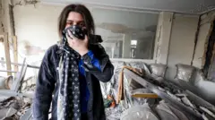 Una mujer imira a cámara cubriéndose la cara con un pañuelo en medio de escombros dentro de su apartamento después de que fuera alcanzado por un ataque aéreo, en Teherán.
