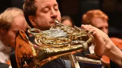 පාදයේ ඇඟිලි වලින් 'ෆ්‍රෙන්ච් හෝන්' වාදනය කරන මිනිසා