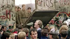 West Berliners crowd in front of the Berlin Wall early 11 November 1989 as they watch East German border guards demolishing a section to open a new crossing point between East and West Berlin