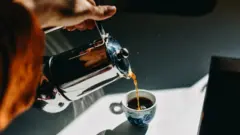 Photo of a woman pouring an espresso cup into a small mug