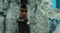 An East German guard peers through a whole in the Berlin Wall