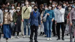Personas caminando en la calle con mascarillas.