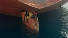 Three people sitting on a ship's rudder