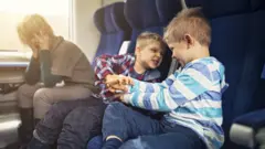 Una mujer en un tren con dos niños traviesos al lado