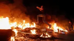 A Palestinian protester jumps over a burning barricade near the West Bank city of Ramallah. Photo: 9 May 2021