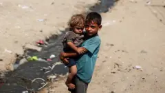 一個加沙男童手中懷抱另一個更小的孩子