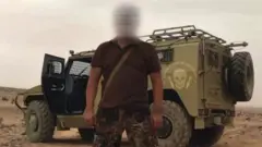 A Wagner soldier stands in front of an armoured vehicle