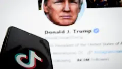 TikTok logo on phone in front of Donald Trump's Twitter feed on a PC screen.