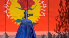 Женщина в парандже на фоне плаката