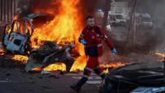 Un rescatista frente a un auto incendiado en Kyiv