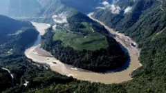 Vista aérea do Rio Yarlung Tsangpo, e uma de suas muitas curvas do rio, mostrando vegetação e picos nas montanhas à distância
