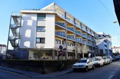 Vista externa de um prédio branco de quatro andares com carros estacionados do lado de fora