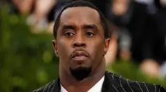 Diddy yi uwe ọcha n'ime ma yikwasị ya uwe 'suit' na-eji oji nwere akara ogologo dị ọcha.