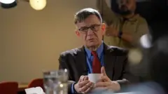 Андрей Ланьков сидит с чашкой во время съемки