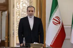 O ministro das Relações Exteriores do Irã, Abbas Araghchi, ao lado da bandeira iraniana; ele veste um blazer preto sobre uma camisa persa branca sem colarinho