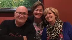 Kevin, Deb e Val sorriem à mesa de um restaurante