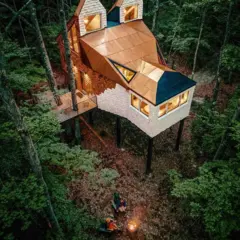 Uma casa sustentada por algumas vigas. A varanda é apoiada em duas árvores. O telhado é de cobre, a parte da frente da parede é de pedra branca, no formato de rosto de uma raposa.