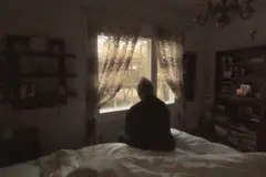 persona sentada en una cama mirando a la ventana