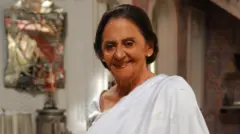 Laura Cardoso sorri para a câmera, vestindo branco, em um ambiente interno.