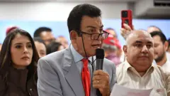 Salvador Nasralla sostiene un micrófono y unos documentos mientras realiza una conferencia de prensa, rodeado de colaboradores, en Tegucigalpa 