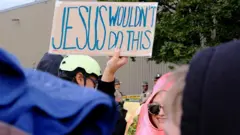 Manifestante segura um cartaz com os dizeres "Jesus não faria isso" em inglês, durante um protesto no lado de fora do centro de detenção do Serviço de Imigração e Alfândega dos Estados Unidos em Broadview, no Estado de Illinois, durante a mais recente batida contra imigrantes no país, no dia 10 de outubro de 2025