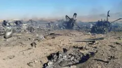 एक तस्वीर में जले हुए हेलिकॉप्टर का मलबा दिख रहा है, जिसके बारे में कहा जा रहा है कि यह ईरान में फँसे अमेरिकी एयरमैन की तलाश के दौरान अमेरिकी मिशन में नष्ट हुआ था. रेतीली ज़मीन पर धातु के टुकड़ों और धुएँ के बीच दो प्रोपेलर जैसे हिस्से नज़र आ रहे हैं.