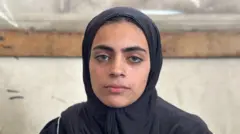 Aya al-Skafi zaune tana kallon kyamara idonta cike da ƙwalla, sanye da baƙaƙen tufafi da hijabi.
