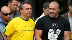 Jair Bolsonaro, vestindo uma camiseta amarela, e Daniel Silveira ao lado, com uma camiseta preta com um desenho de uma mão apontando uma arma, em uma foto de 2022.