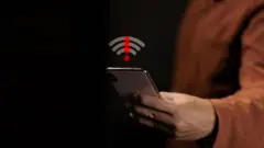 Hand holding mobile phone showing wireless signal problem with red exclamation mark. Concept of no internet connection, network error, system failure and offline status.