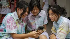 Seorang siswa SMP, gadis berusia 14 tahun (kiri), dan teman-temannya menonton TikTok di smartphone setelah kegiatan sekolah pada tanggal 27 Maret 2026 di Yogyakarta