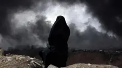 Vista pelas costas, uma mulher usando um chador observa a paisagem enquanto uma fumaça preta se espalha pelo horizonte
