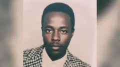 An old passport photo of Biniam Solomon, He is wearing a dog-tooth jacket and white shirt.