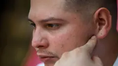 Andy Perozo apontando para a orelha esquerda. Ele afirma que os guardas faziam barulho à noite para impedir que os migrantes dormissem