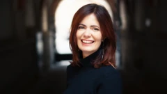 Ilana Eleá em uma foto olhando para a câmera e sorrindo. Ela tem cabelos escuros, lisos, na altura dos ombros e veste uma blusa escura.