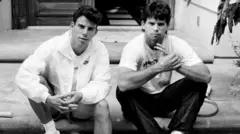 Os irmãos Menendez, Erik (à esquerda), e Lyle nos degraus de sua casa em Beverly Hills em novembro de 1989, em uma foto em preto e branco.