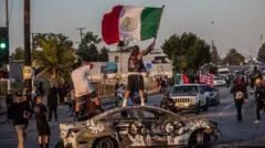Manifestantes en Paramount sobre un auto quemado.