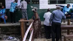  Wapiga kura wakiangalia majina yao kwenye daftari la wapiga kura katika kituo kinachosubiri kufunguliwa huko Kinshasa mnamo Desemba 20.