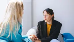 Duas mulheres sentadas uma de frente para a outra conversam.