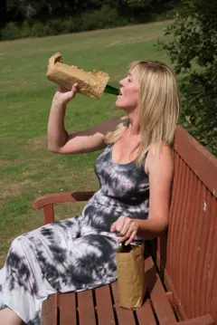 Mulher bebendo álcool com uma garrafa dentro de um saco de papel pardo em um local público