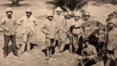 Ancient French colonial masters wear boots and oversize coats dey pose for a photo