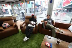 Austin Franklin (desno) in Kevin Akoto gledata tekmo svetovnega prvenstva 2026 med Portugalsko in Uzbekistanom iz svoje prozorne kocke na Times Squareu v New Yorku 23. junija 2026.