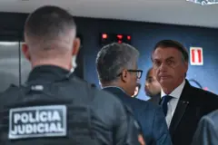Agente com farda da Polícia Judiciária de costas; Bolsonaro é visto em pé e com olhar tenso, rodeado por outras pessoas