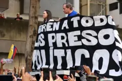 Líderes da oposição venezuelana, María Corina Machado e Juan Pablo Guanipa seguram faixa pedindo a liberdade dos presos políticos no país