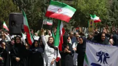 Медицинские работники, держащие иранские флаги, принимают участие в акции протеста против американо-израильских ударов по медицинским учреждениям у больницы имени имама Хомейни в Тегеране, Иран, 6 апреля 2026 года.