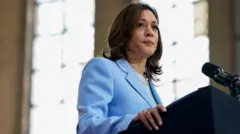 Kamala Harris porte un costume bleu et semble hors cadre alors qu'elle se tient devant un microphone.