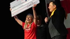 マスク氏から100万ドルの小切手を贈られ喜ぶ、トランプ候補支持のTシャツを着た女性（20日、ペンシルヴェニア州ピッツバーグ）