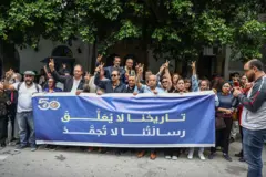 عدد من الناشطين الحقوقيين التونسيين يمسكون بلافتة زرقاء ممتدة كُتب عليها باللون الأصفر والأبيض "تاريخنا لا يُعَلَّق، رسالتنا لا تُجمَّد"، بينما يرفع بعضهم علامة النصر.